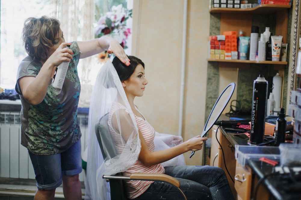 Best beauty parlour in Thodupuzha providing bridal hair styling as a professional stylist sets a bride’s veil and hairstyle in a salon while she looks into a mirror.